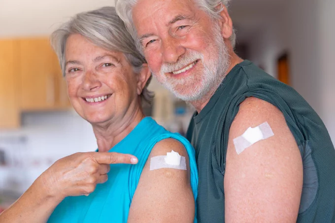 Smiling older couple with their sleeves rolled up and bandaids on their upper arms